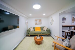 A living room with a green sofa, a wooden coffee table, and a TV mounted on the wall. - Gateway to Nyc! Modern & Cozy Unit (Bayonne)