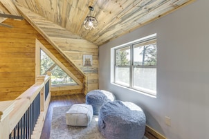 Una habitación con techo inclinado, vigas de madera, un ventanal grande y una obra de arte con temática de oso.