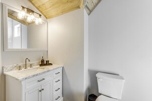 Un baño con encimera de mármol, un lavabo con grifo, un espejo con iluminación, un inodoro y un techo de madera.
