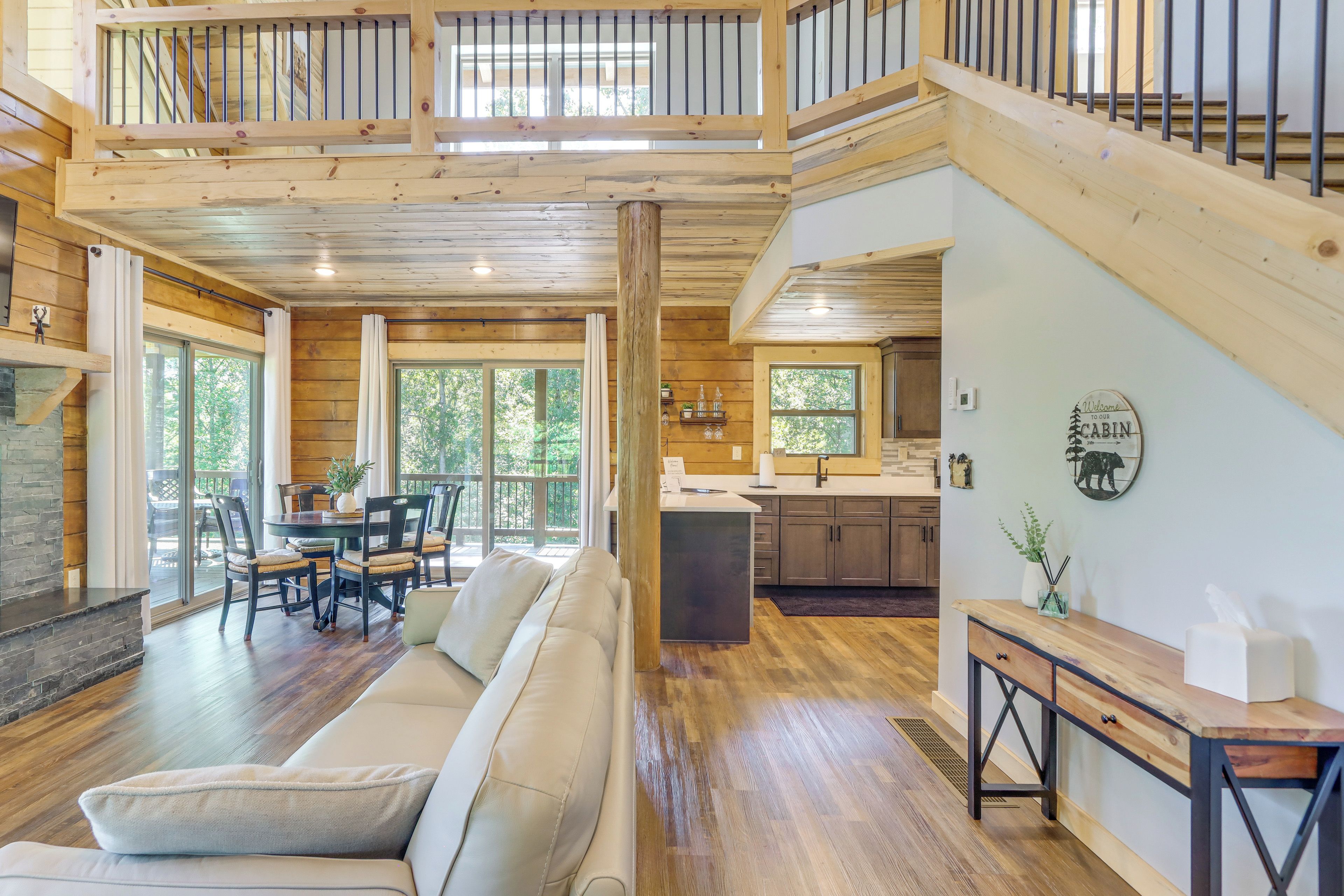 A spacious living area with a sofa, dining table, and chairs, a kitchen with a sink and cabinets, and a staircase leading to an upper level.