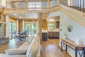 A spacious living area with a sofa, dining table, and chairs, a kitchen with a sink and cabinets, and a staircase leading to an upper level. - Mtn-view Deck! Ellijay Escape, Hike, Bike & Fish (Ellijay)