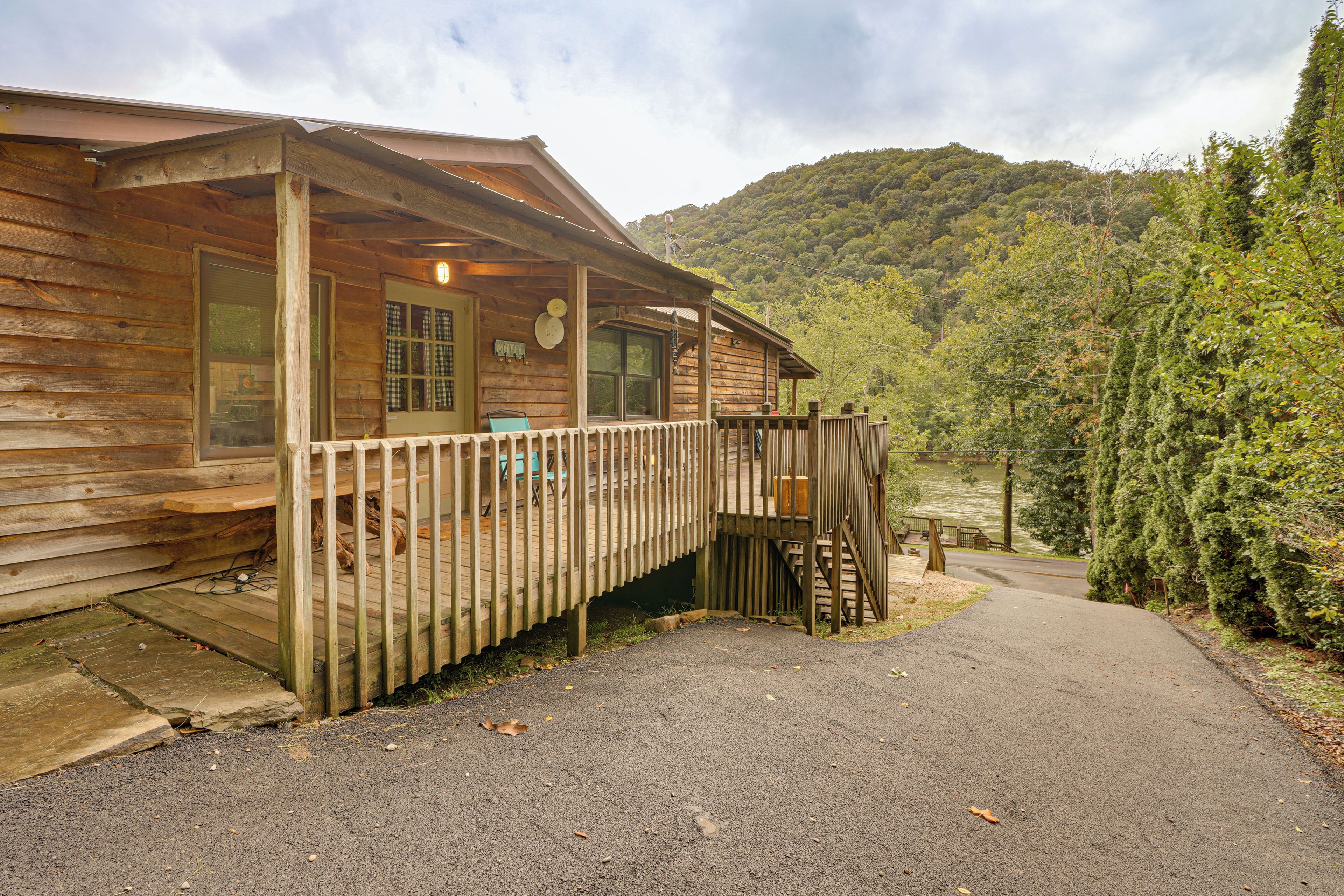 A wooden cabin with a porch, a deck, and a view of a forested hillside.