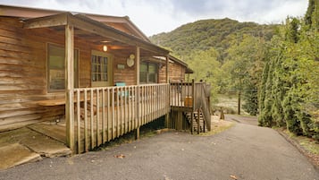 A wooden cabin with a porch, a deck, and a view of a forested hillside.
