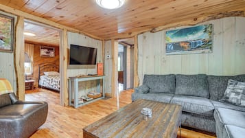 A cozy cabin interior with a wooden floor, a sofa, a chair, a television, and a painting on the wall.