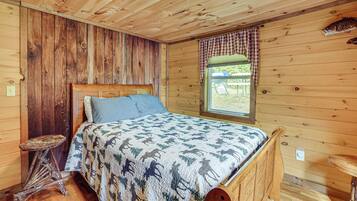 A wooden room with a bed, a window with curtains, and a rustic wooden table.