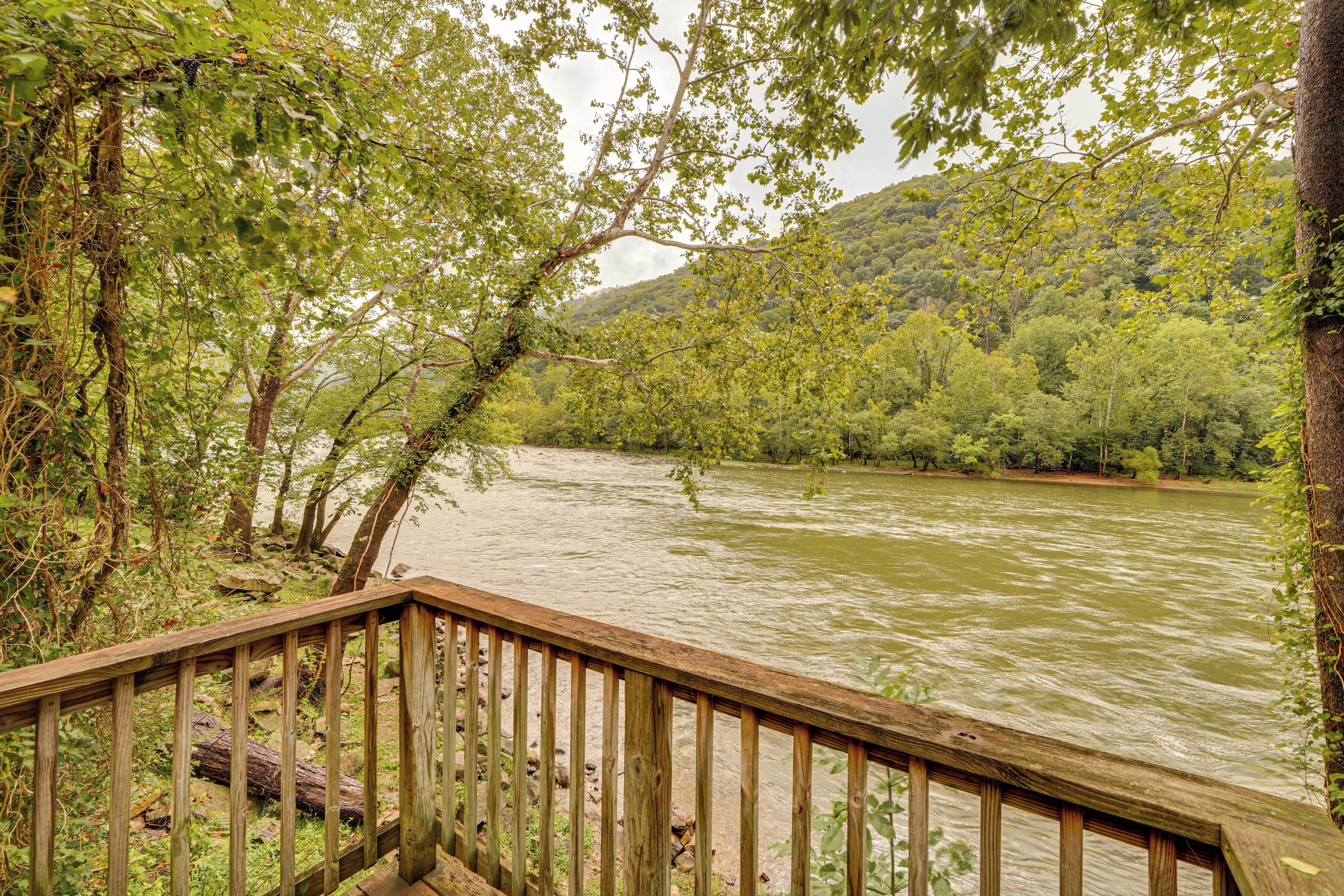 A wooden deck overlooking a river with dense greenery and hills in the background.