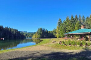 Vista de un lago con un pabellón, mesas de picnic y cielo despejado.