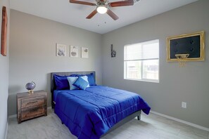 Ein Schlafzimmer mit Bett, Nachttisch, Globus, Deckenventilator und einem Fenster mit Jalousien.