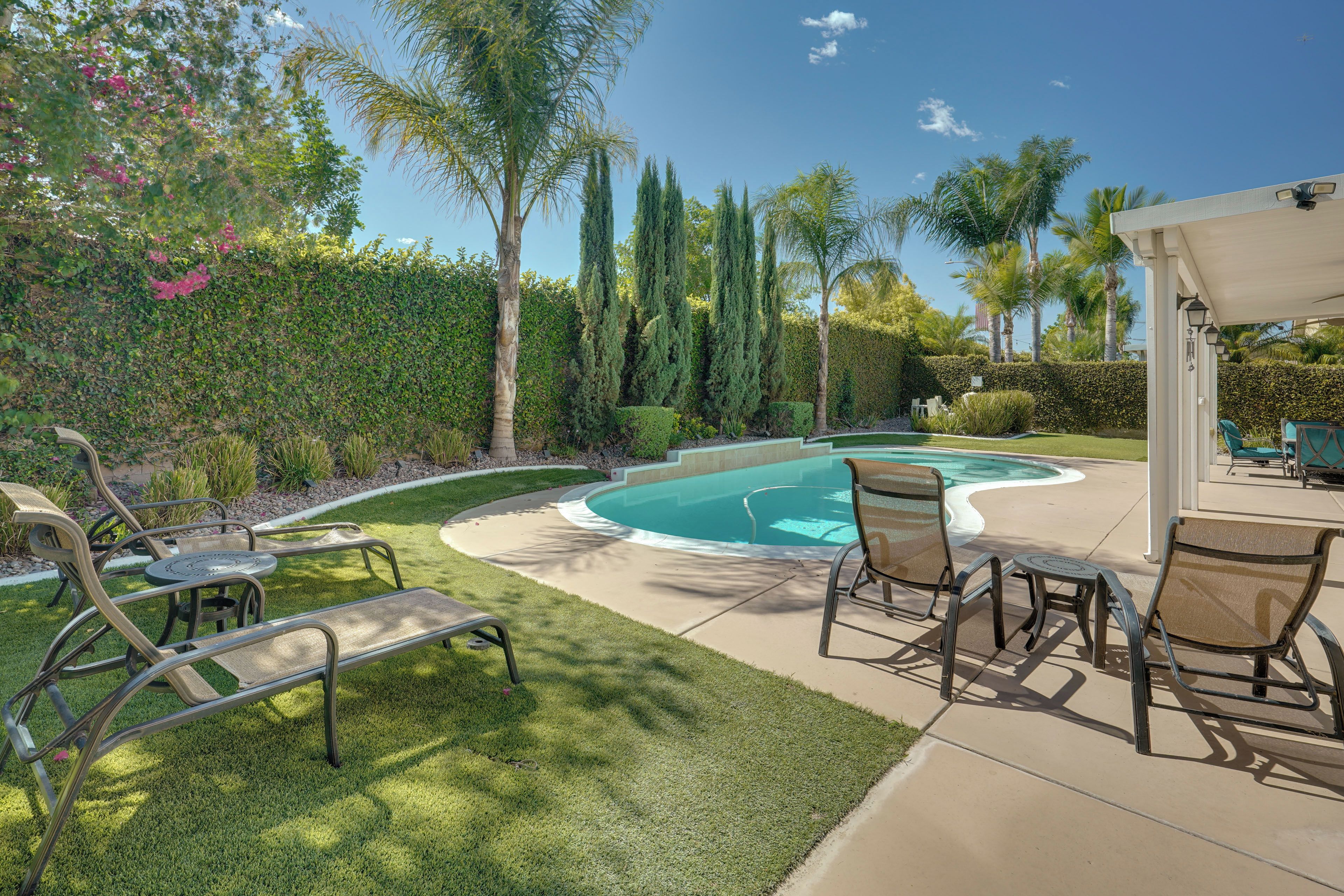 A backyard with a swimming pool, lounge chairs, and a covered patio area.