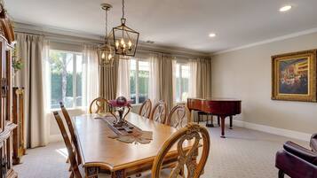 A dining room with a wooden table, chairs, a piano, and a painting on the wall.