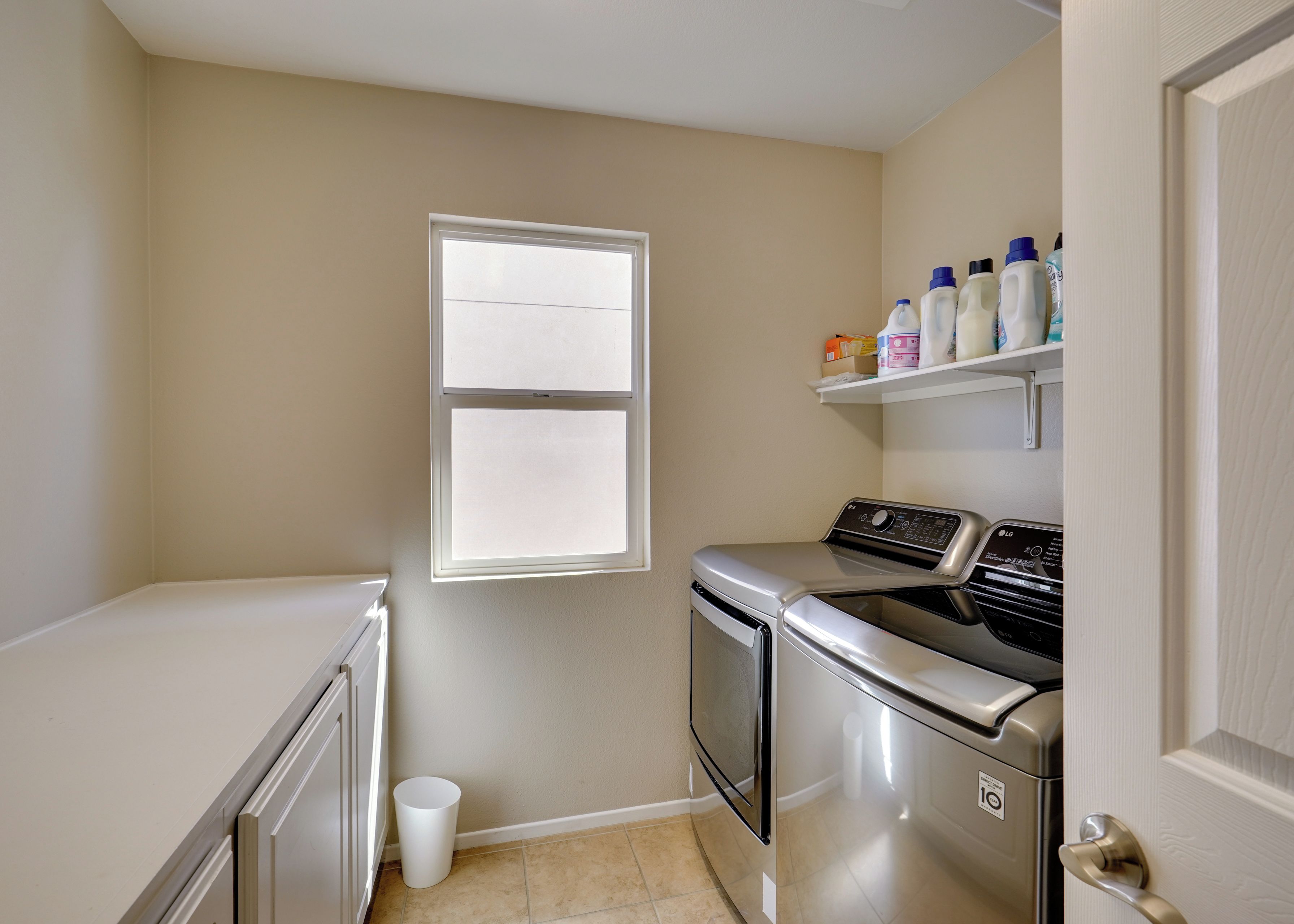 A laundry room with a washing machine, dryer, and a shelf with cleaning supplies.