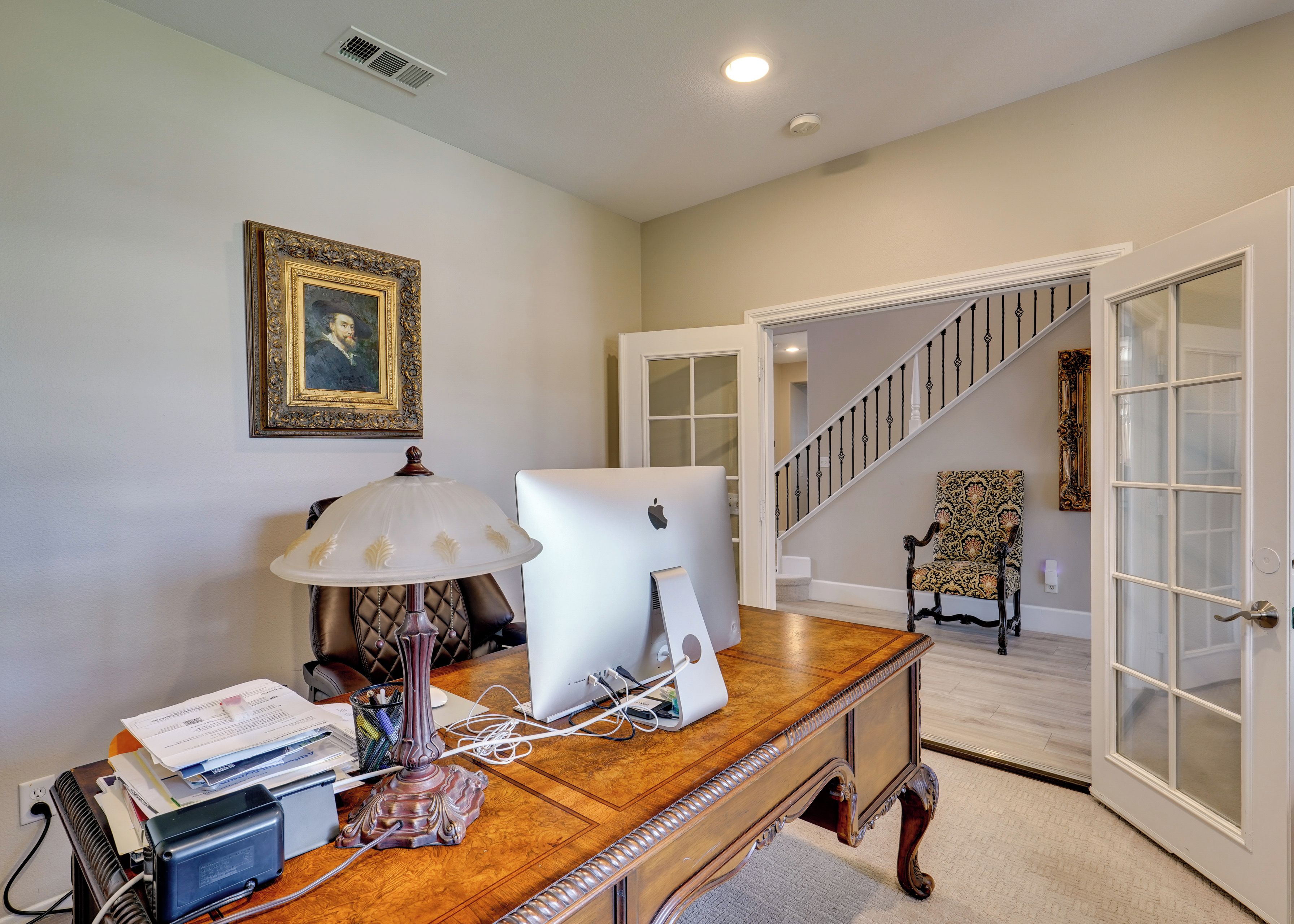 A home office with a desk, computer, lamp, and a framed picture on the wall.