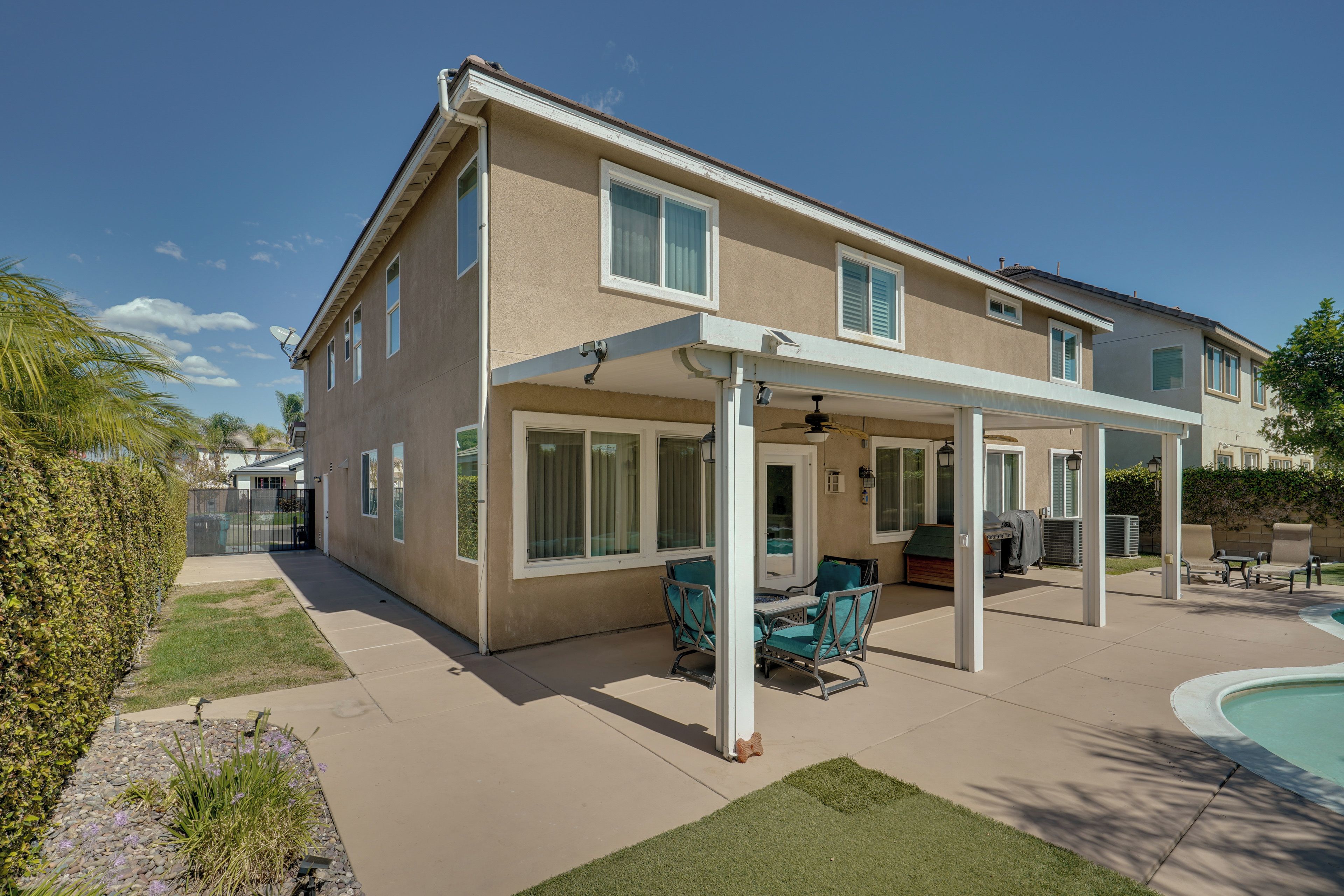 A two-story house with a covered patio area, a pool, and a well-maintained lawn.