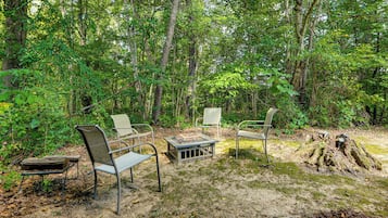 Een terras met metalen stoelen en een tafel, omgeven door bebossing.