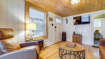 Un salon chaleureux avec un canapé en cuir, une table basse ronde et un téléviseur à écran plat fixé au mur.