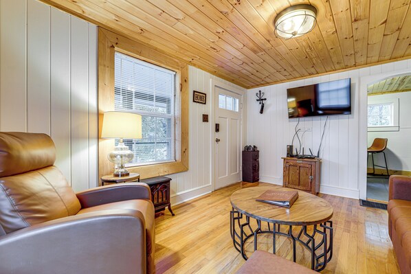 A cozy living room with a leather sofa, a round coffee table, and a flat-screen TV mounted on the wall. - Cozy Candler Cottage, Near Hiking and Wildlife (Candler)