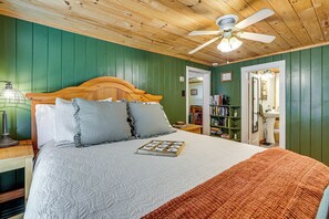 Une chambre à coucher avec une tête de lit en bois, un lit avec une couette et des oreillers, un ventilateur de plafond, une table de chevet avec une lampe et une bibliothèque.