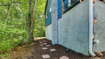 A pathway leading to a house with a blue exterior and brick foundation, surrounded by a forested area.