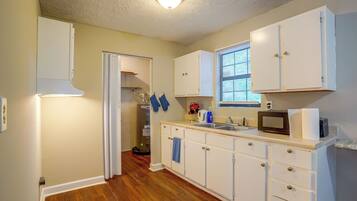 A kitchen with white cabinets, a wooden floor, a window with blinds, and a microwave on the counter.