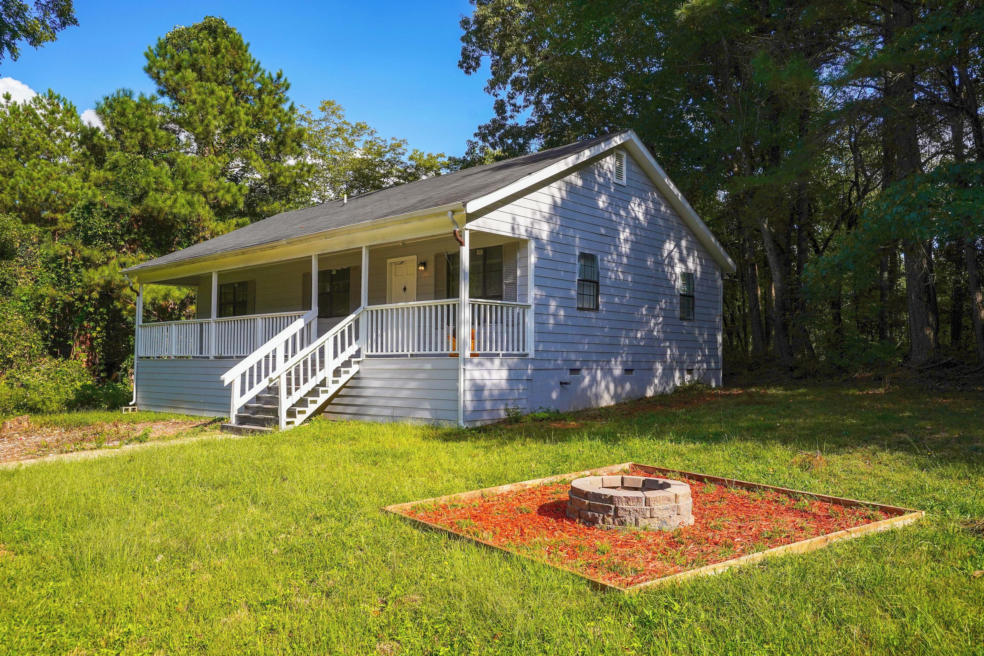 A single-story house with a porch, a staircase, and a fire pit in the yard.