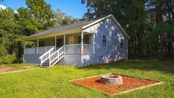 A single-story house with a porch, a staircase, and a fire pit in the yard.
