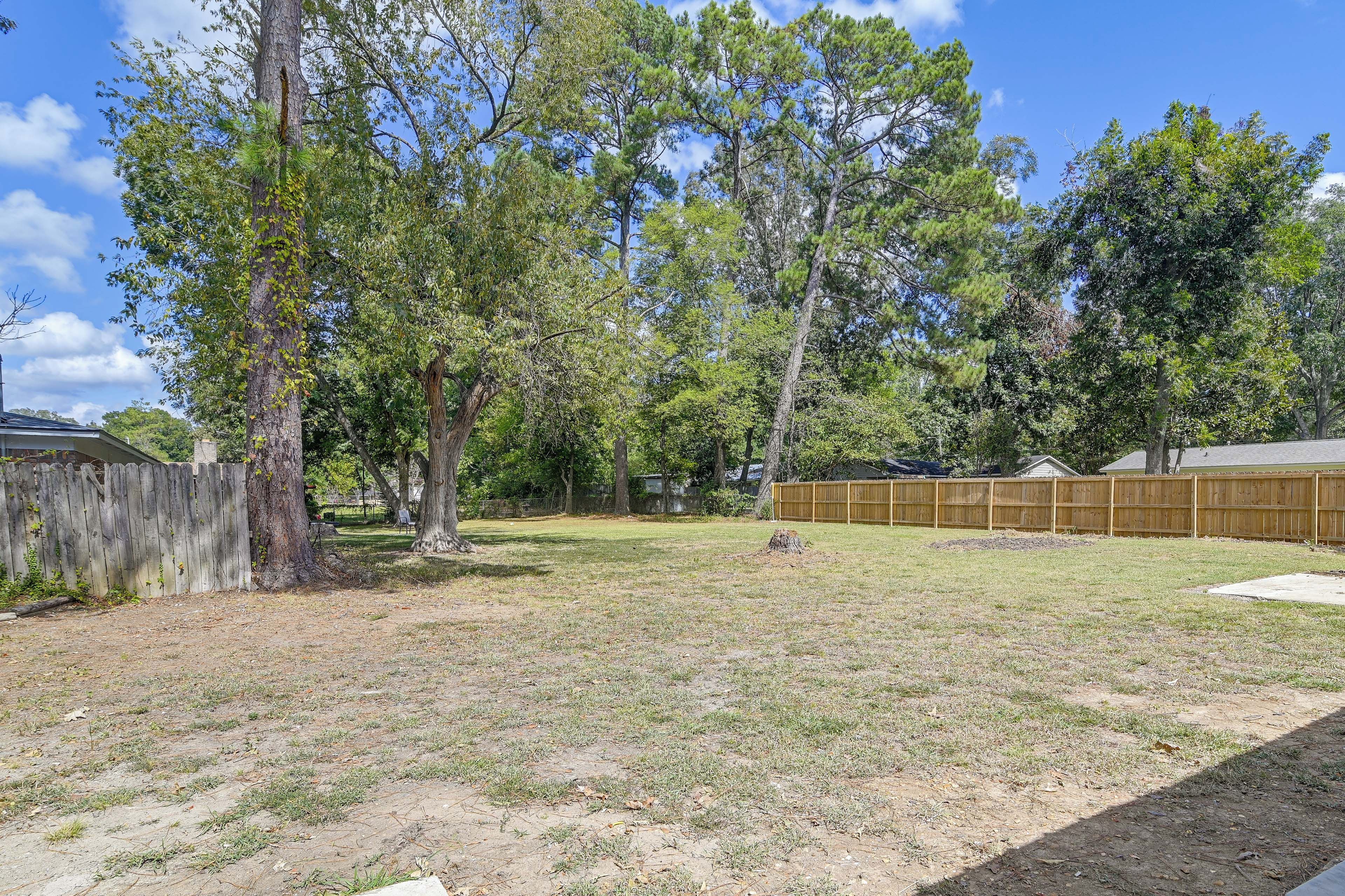 A backyard with a wooden fence, trees, and a grassy area.