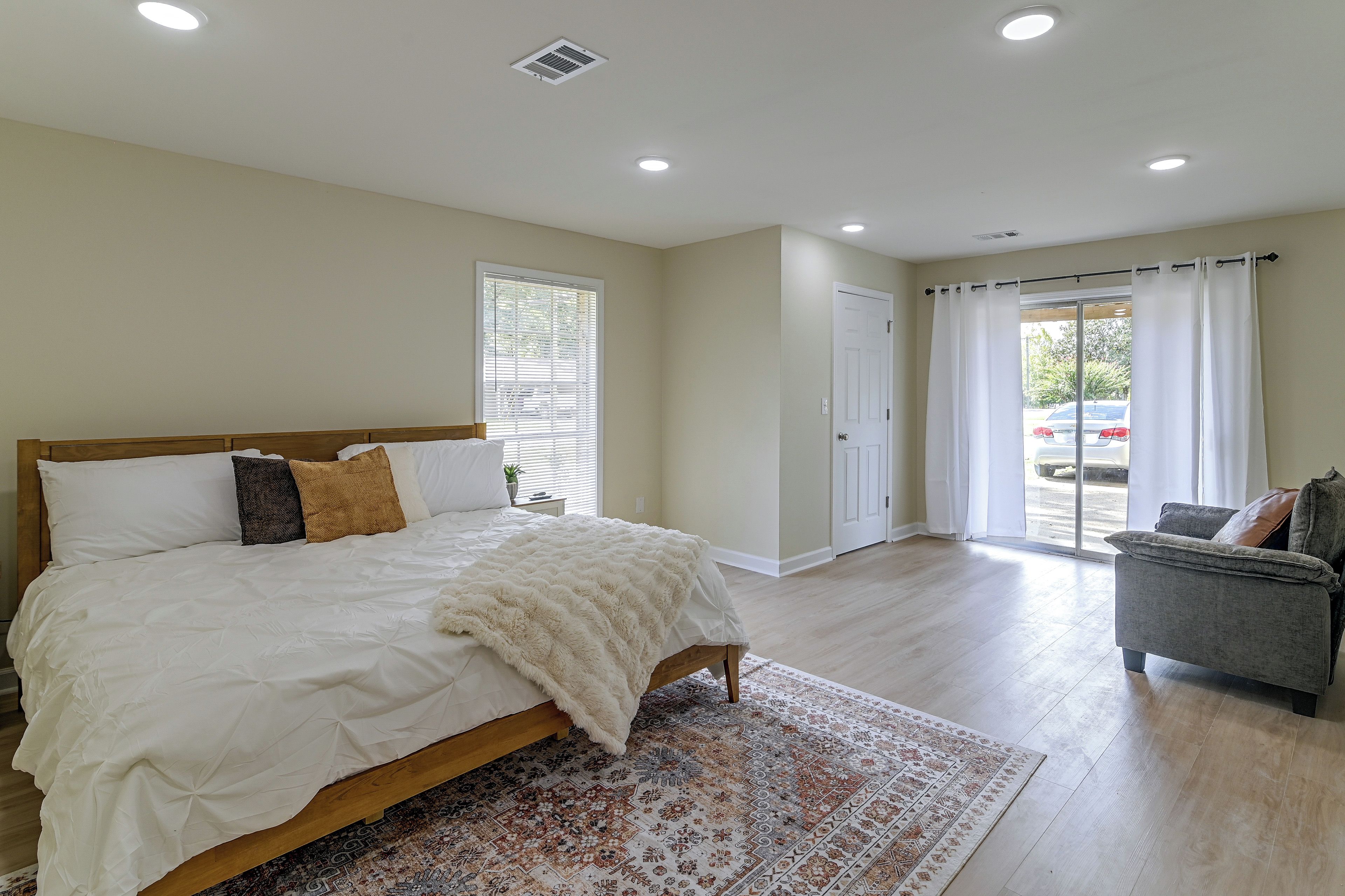 A bedroom with a bed, a window with blinds, a door, and a view of the outside.