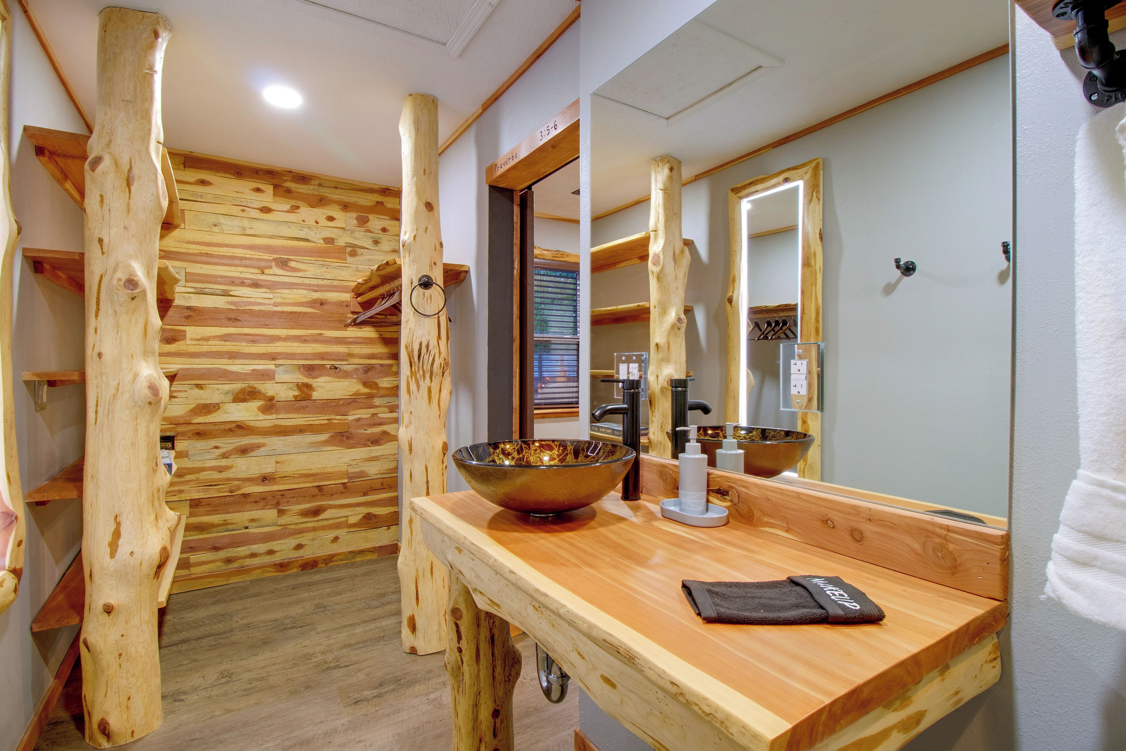 A bathroom with wooden paneling, a large mirror, a wooden vanity, and a bowl sink.