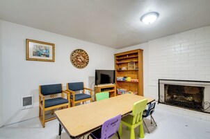 Una habitación con una mesa de madera, dos sillas, un televisor, una estantería y una chimenea.