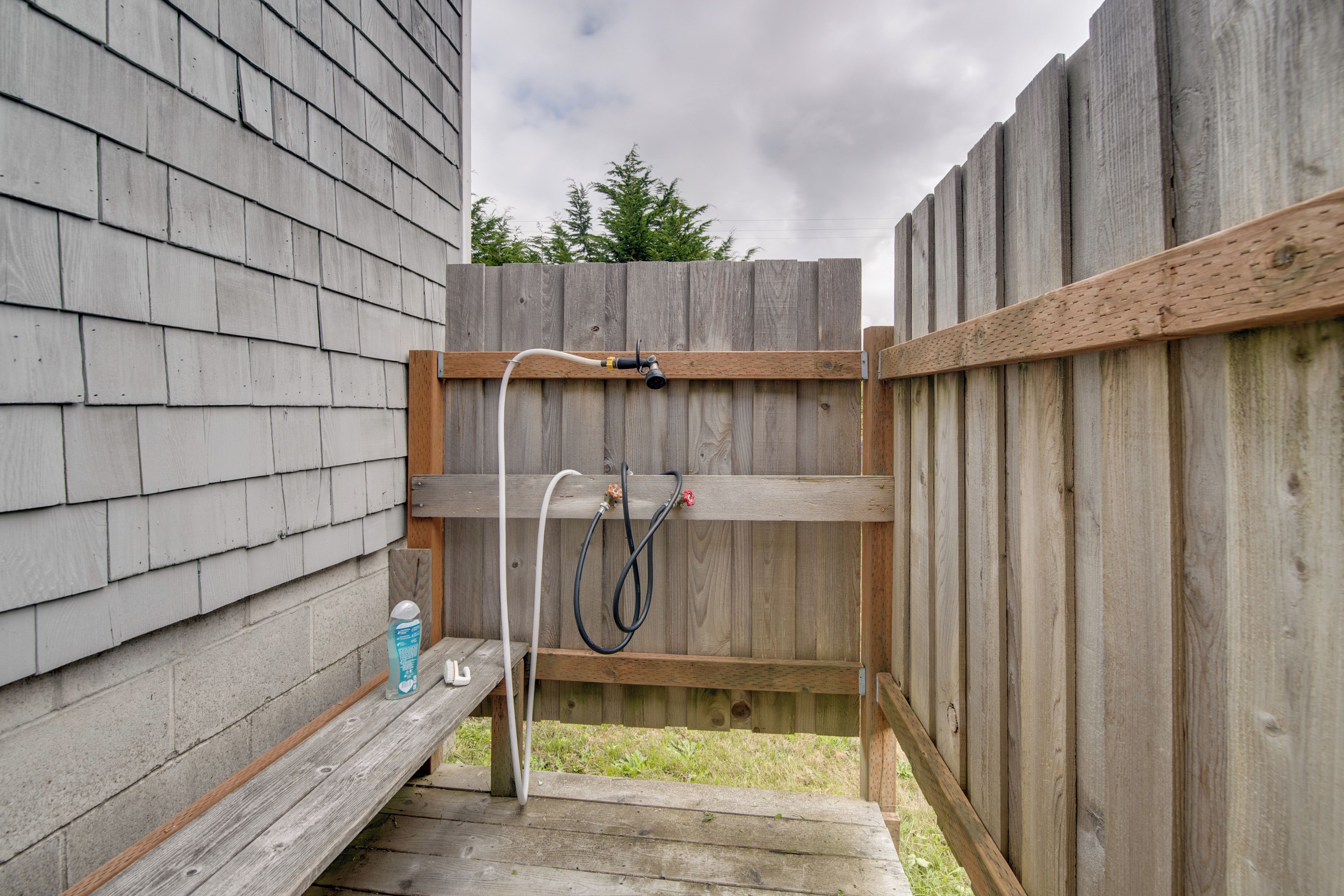A wooden deck with a hose and a bottle, a wooden fence, and a grassy yard.