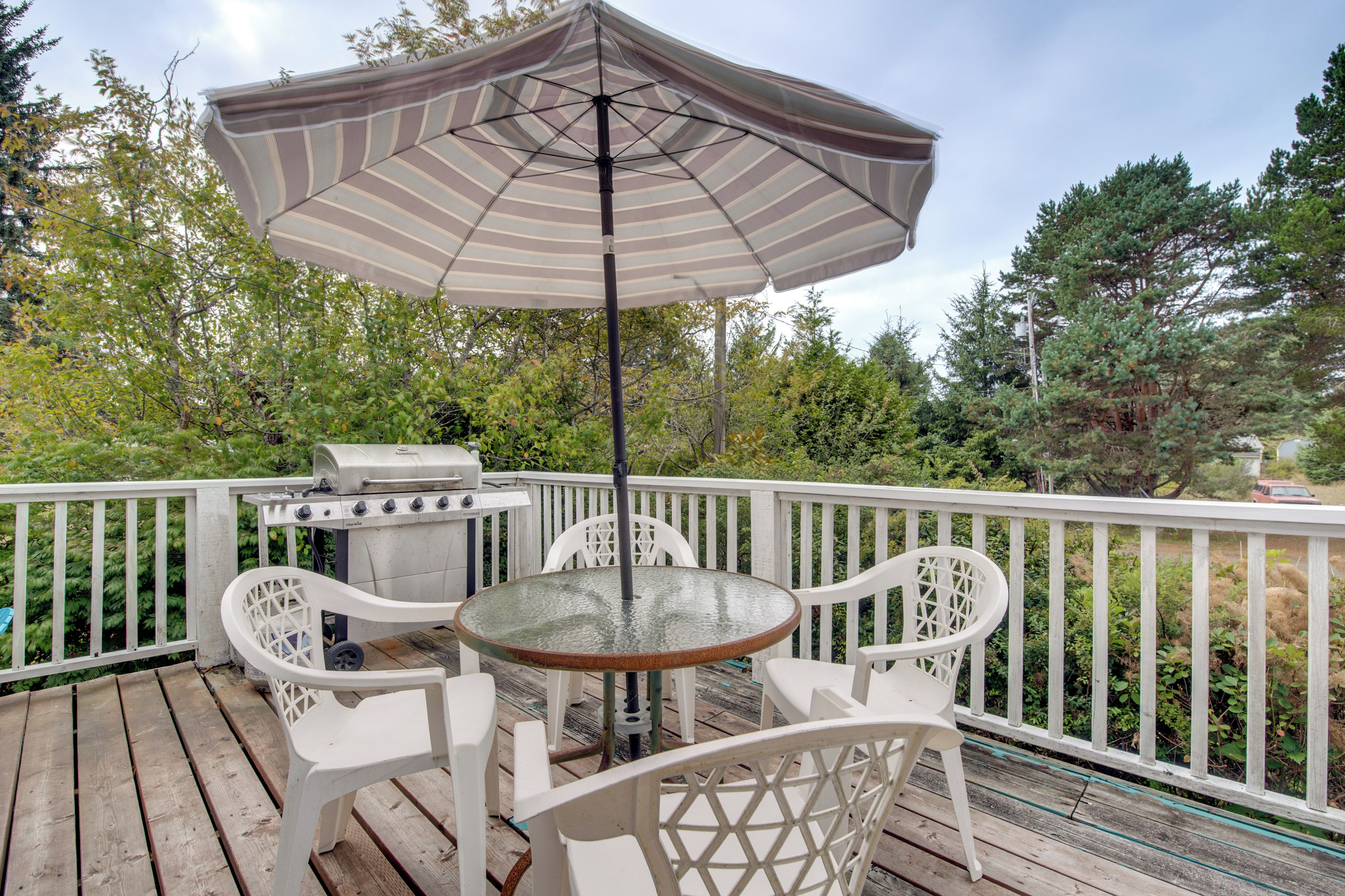A wooden deck with a round table and chairs, a grill, and an umbrella.