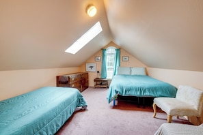 Un dormitorio acogedor en el ático, con dos camas individuales, una silla, un aparador y un tragaluz.