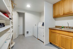 A compact kitchen with white cabinets, a built-in washing machine, and a granite countertop. - Half-mile to Beach! Coastal Washington Hideaway (Grayland)