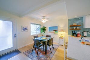 A dining area with a glass table and chairs, a ceiling fan, a window with blinds, and a kitchen with a sink and shelves. - Closest Unit to Beach on Little Gasparilla Island (Placida)