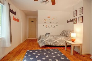 A bedroom with a bed, a nightstand, a lamp, a star-patterned rug, and wall decorations including sports and dinosaur decals. - 'La Massaria' Country Chalet w/ Fall Foliage Views (Ossipee)
