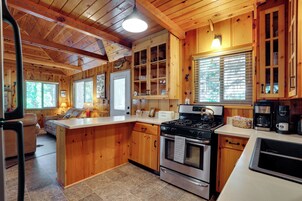 Interior de una cabaña de madera con cocina equipada, que incluye estufa, horno y cafetera.