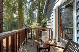 Terraza de madera con mesa y sillas, con vista a un área boscosa.