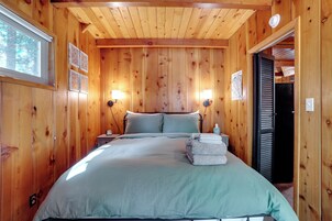 Un dormitorio con paneles de madera, una cama, dos lámparas de noche y un ventanal.