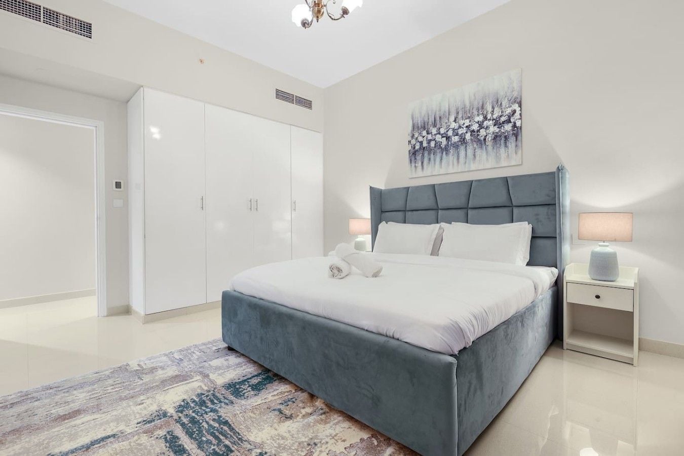 A modern bedroom with a large bed, a wardrobe, a nightstand, and a painting on the wall.