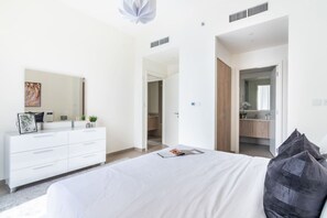 A modern bedroom with a large bed, a dresser, a mirror, and a walk-in closet. - FIRST CLASS |1BR| Luxury Near Dubai Hills Mall (Dubai Hills)