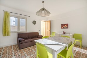 Una habitación con un sofá marrón, una mesa con sillas, un reloj y un cuadro en la pared.