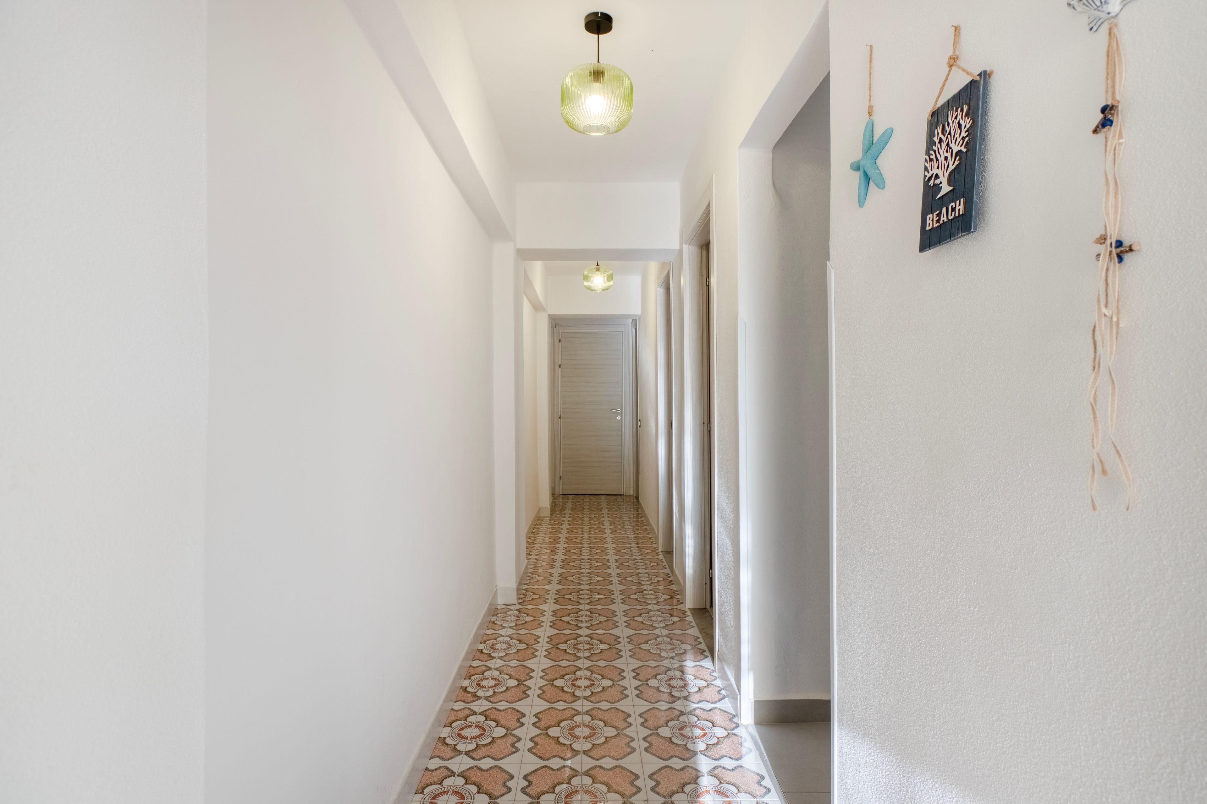 A hallway with patterned floor tiles, a ceiling light fixture, and wall decorations including a starfish and a sign that says 'BEACH'.