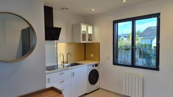 Une cuisine compacte équipée d’un lave-linge intégré, d’un miroir rond et d’une fenêtre donnant sur l’extérieur.