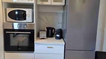 Una cocina compacta con microondas, horno, tostadora, hervidor y refrigerador.