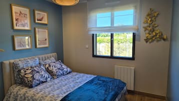 Une chambre à coucher avec un lit, des tableaux encadrés accrochés au mur, une fenêtre donnant sur un paysage et un radiateur.