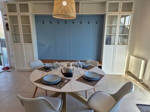 Een eetruimte met een ronde tafel voor vier personen, omringd door witte stoelen, met een blauwe muur en witte kasten op de achtergrond.