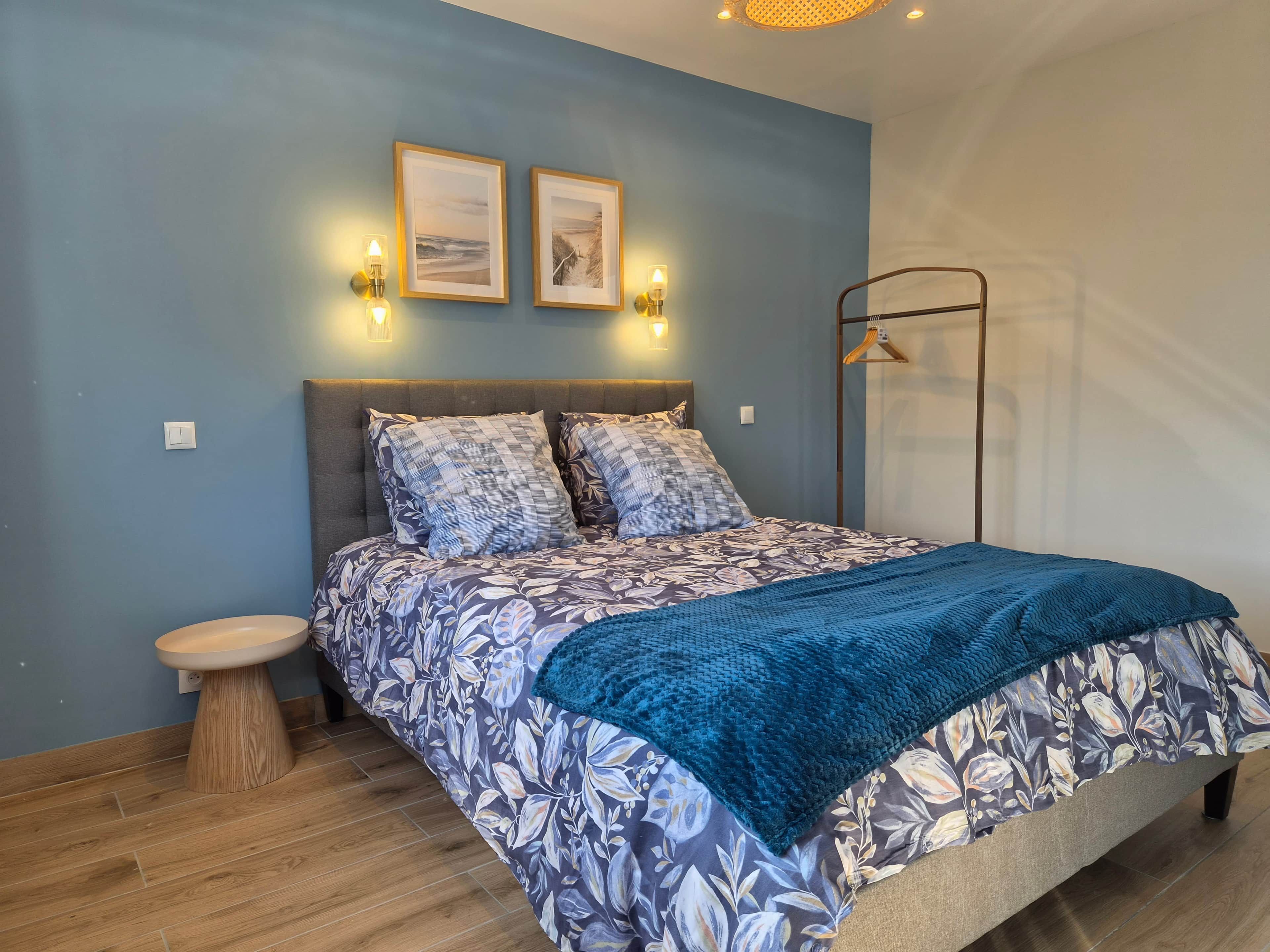 Une chambre à coucher avec un lit, une table de chevet, une lampe fixée au mur et un cadre photo.