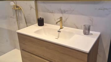 Une salle de bain avec un lavabo blanc, des robinetteries dorées, un meuble-lavabo en bois et un miroir qui reflète la pièce.