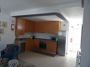 Cocina compacta con armarios de madera, microondas, refrigerador y lavavajillas.