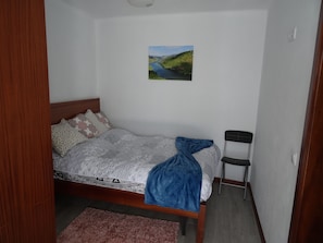 A bedroom with a bed, a chair, a picture on the wall, and a small rug.